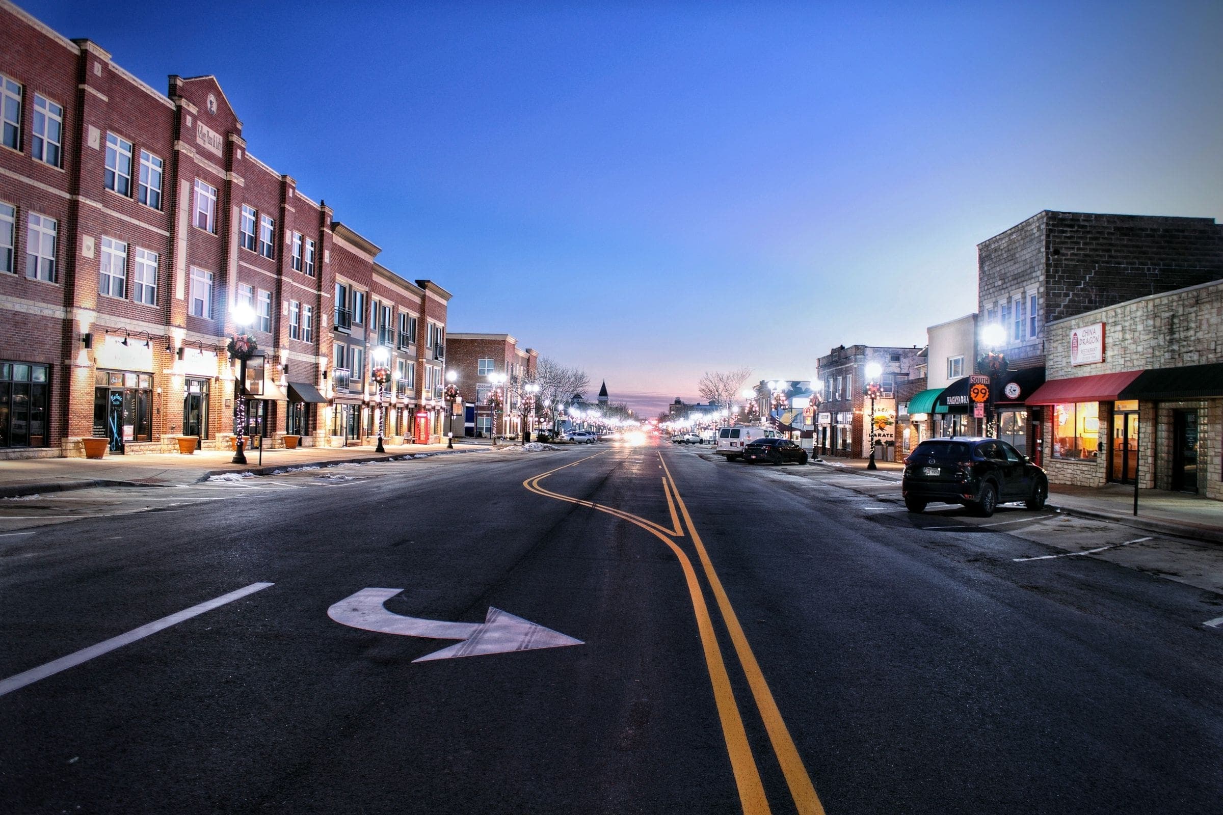 A small-city main street at dusk with lights on