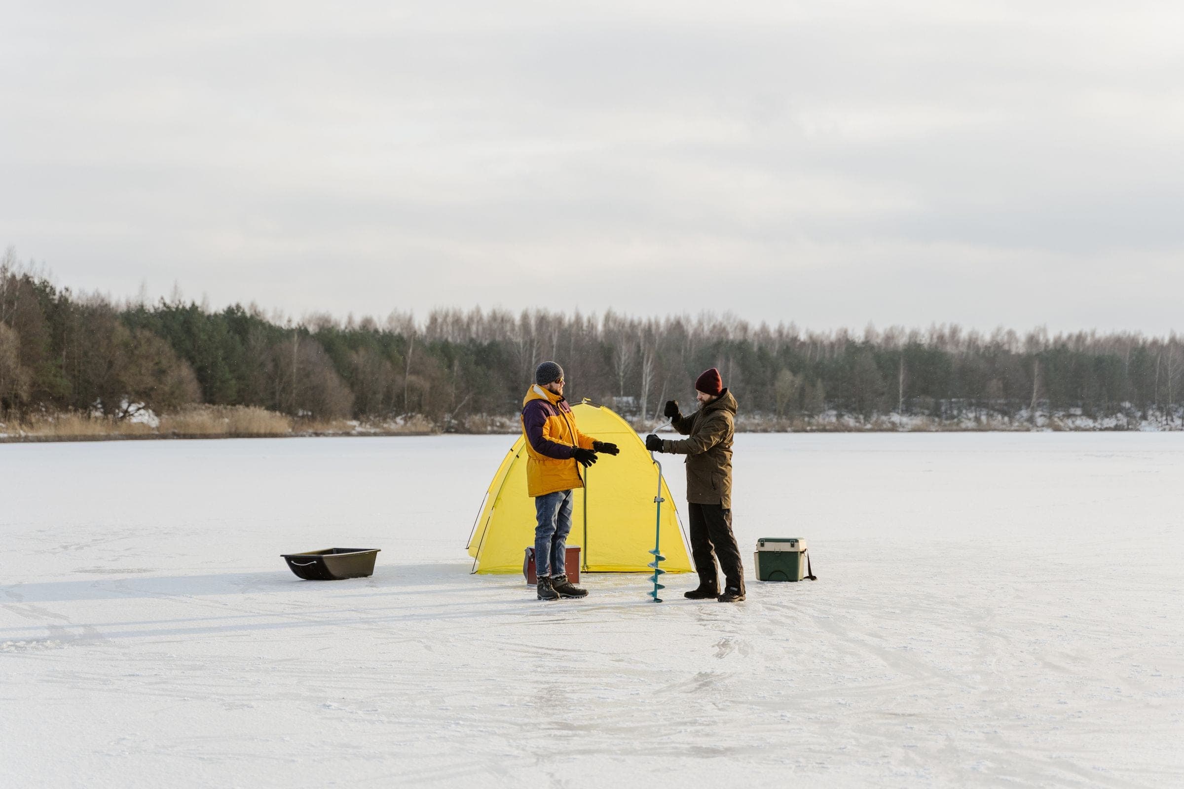 Two anglers ice fishing beside a yellow tent on a frozen lake