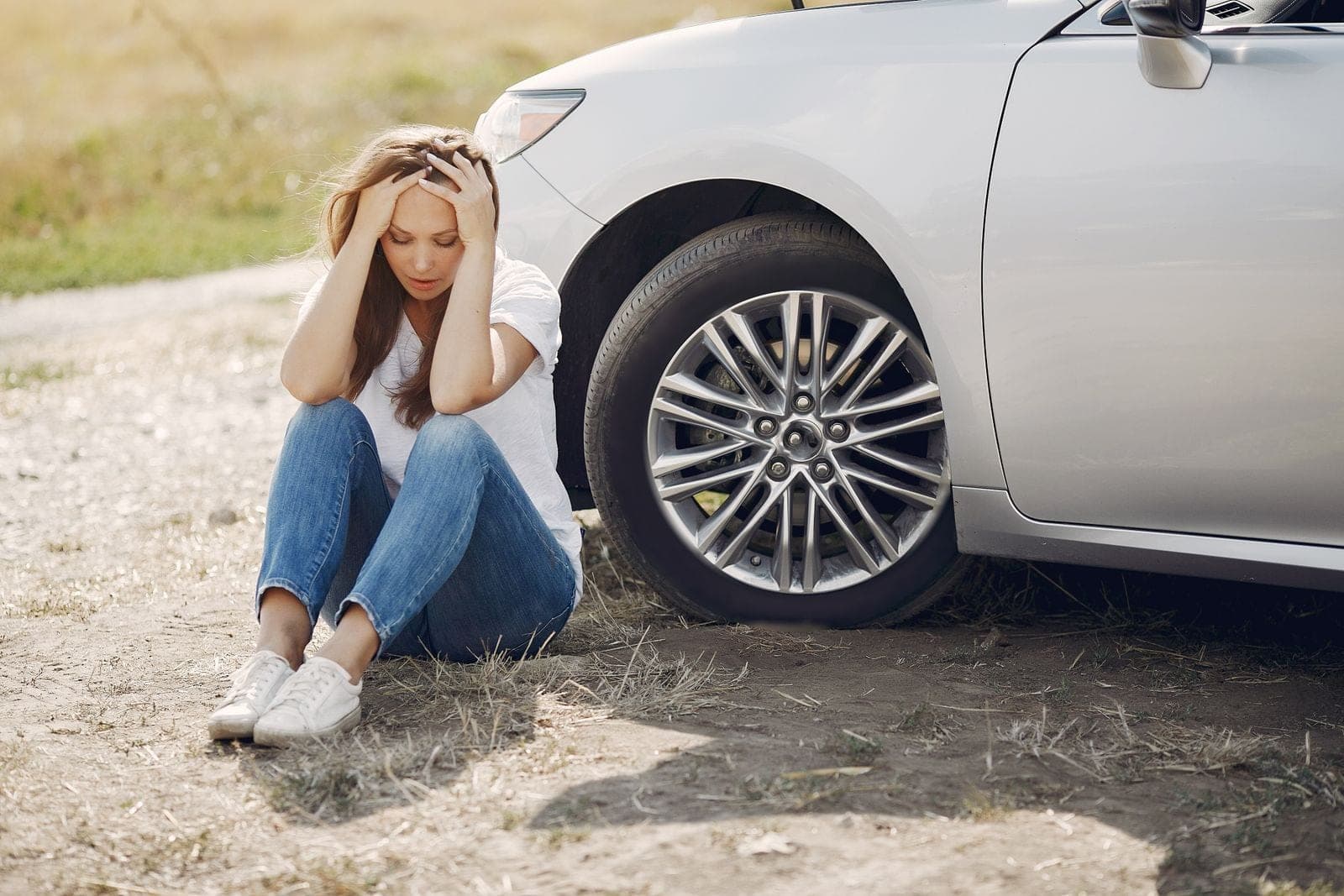 Driver sitting beside a car with a flat tire