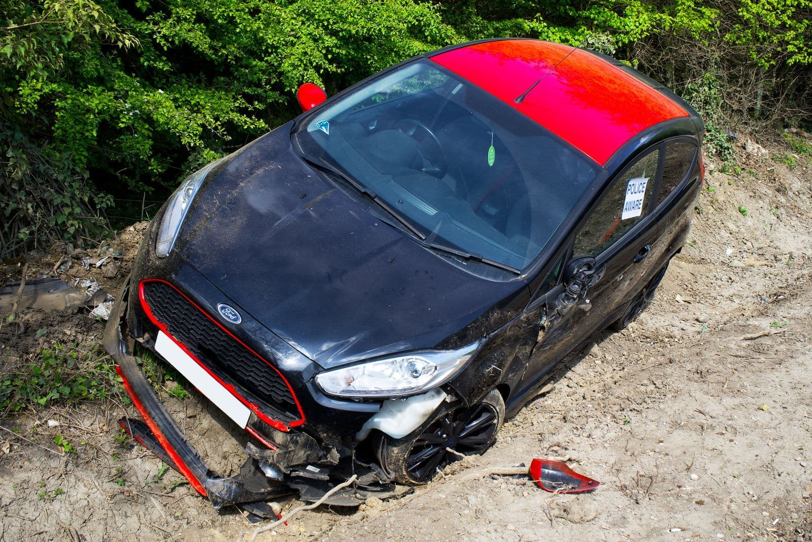 A black and red Ford Fiesta lies abandoned and damaged off-road