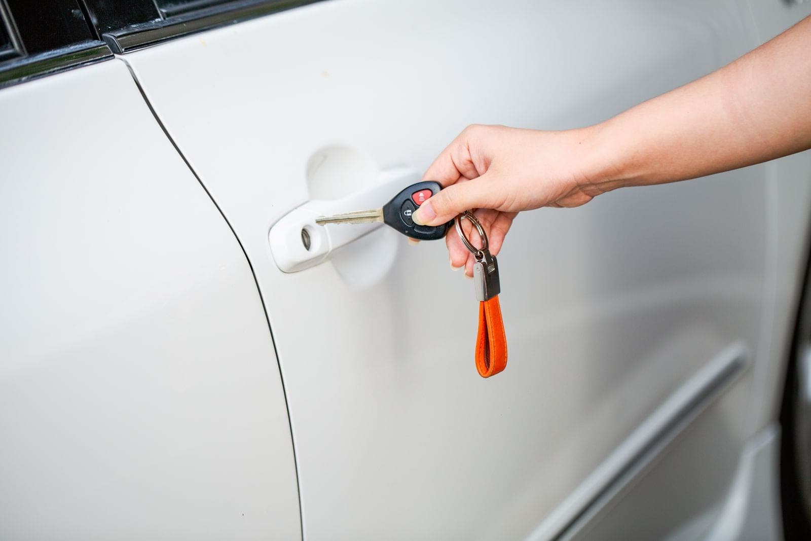 A hand unlocking a white car door with a metal key and key fob.