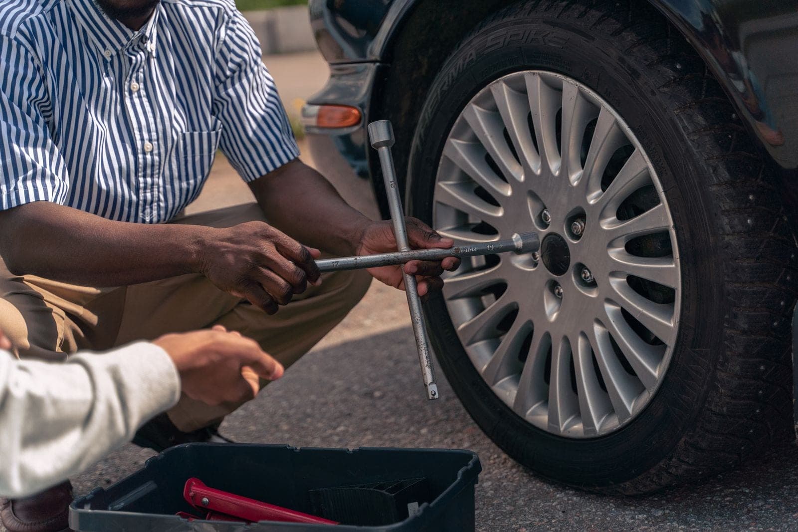 An adult demonstrating how to change a tire to a teenager