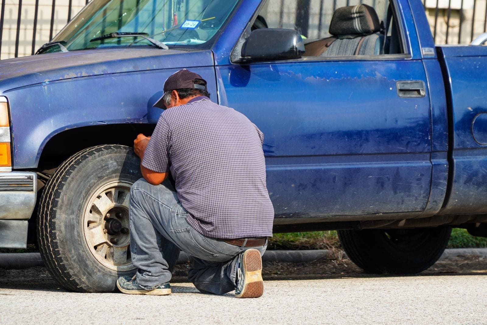 A man attentively repairing a flat tire on a blue truck