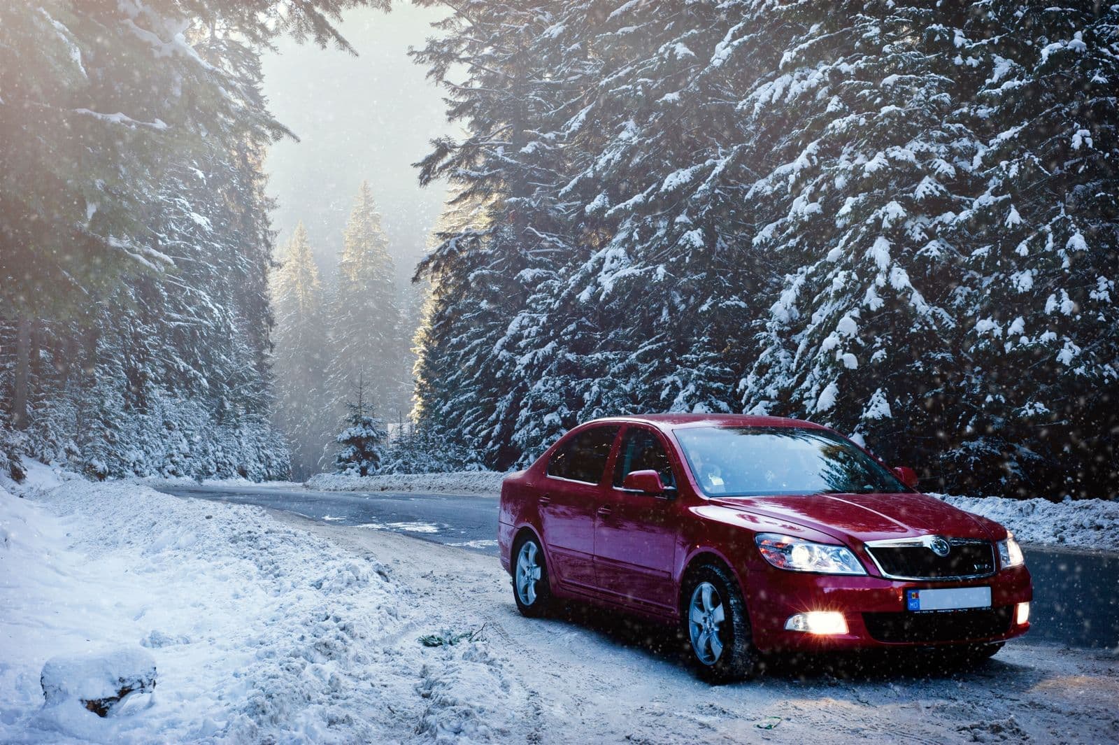 A red car drives along a snowy forest road