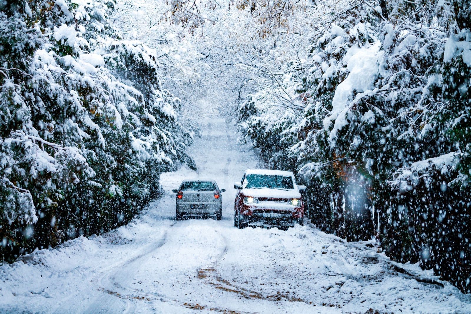 Two cars navigating a heavily snow-covered path