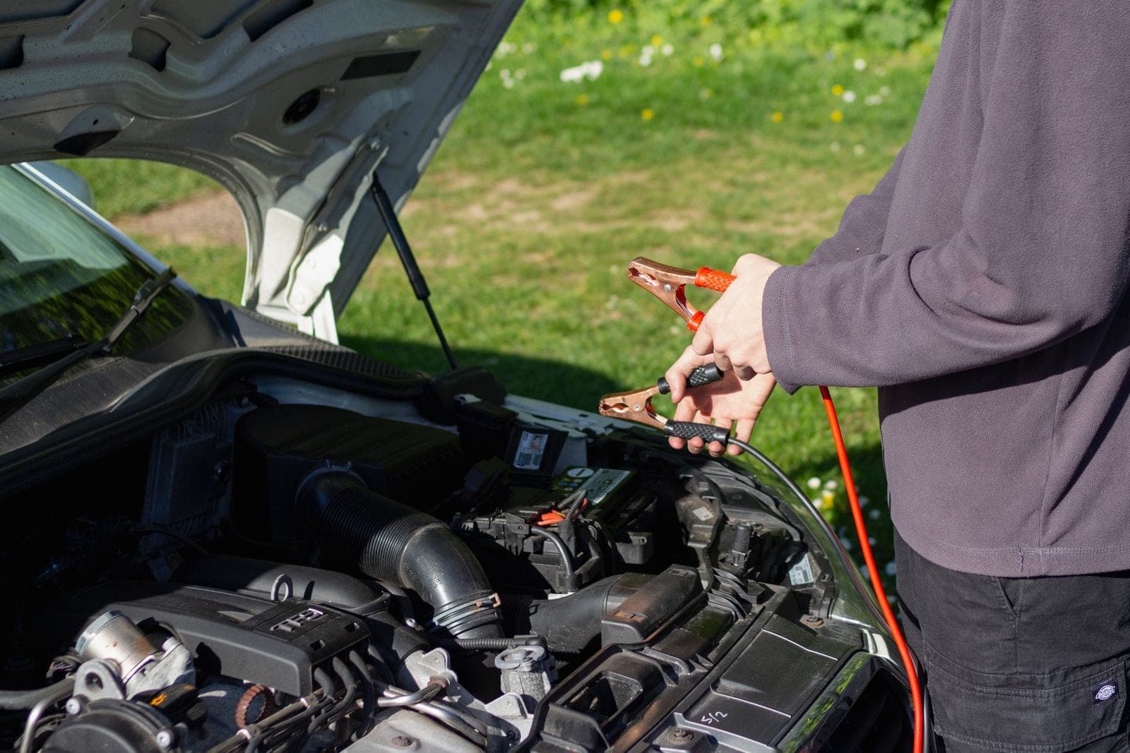 Man connecting jumper cables to a car engine outdoors