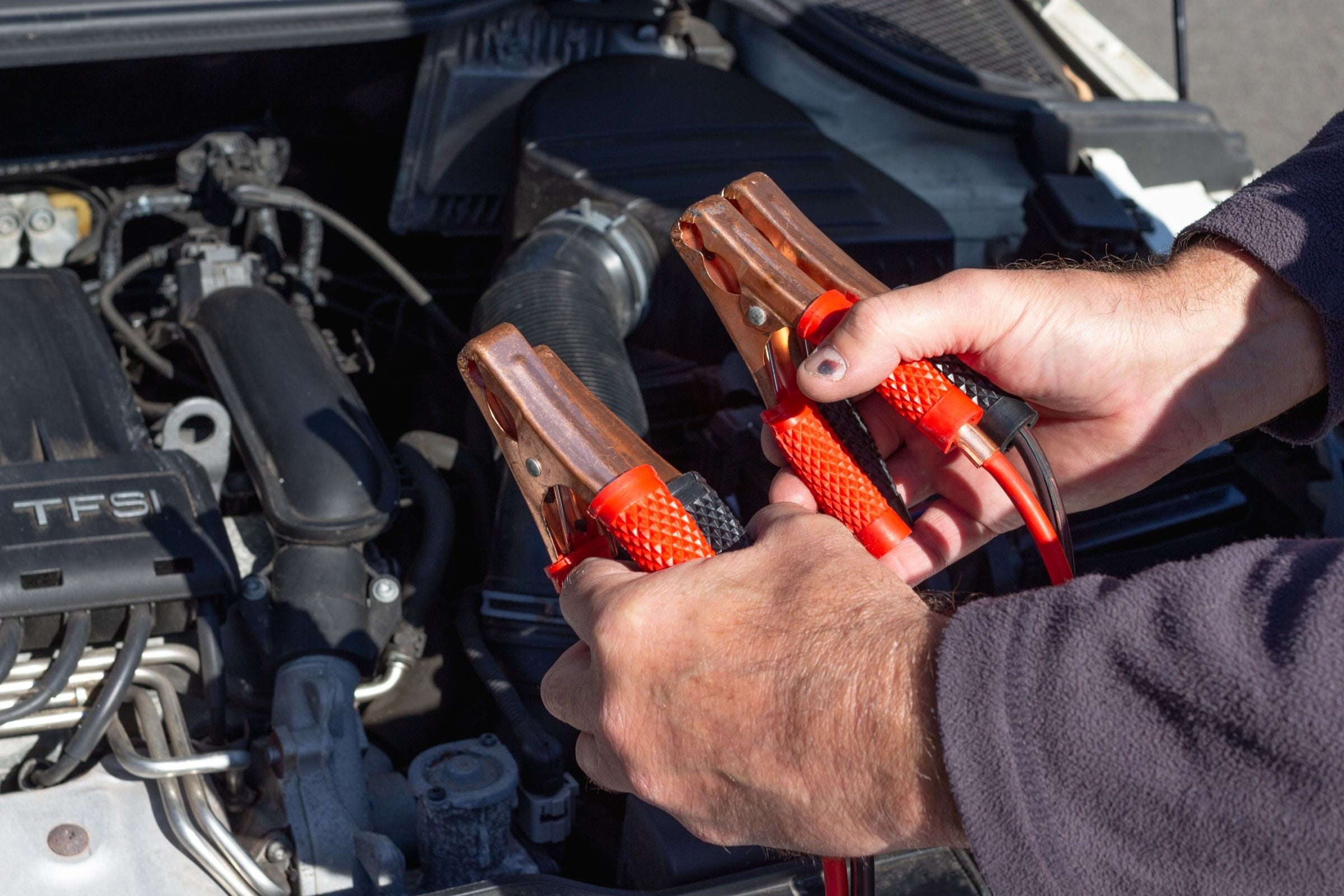 Jumper cable clamps held over an engine during roadside assistance